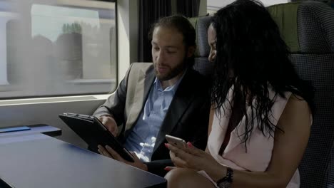 Young-attractive-couple-smiling-and-having-fun-watching-funny-content-on-digital-tablet-while-they-traveling-by-train