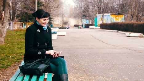 Junge-Frau-mit-Smartphone-auf-einer-Bank-im-Stadtpark