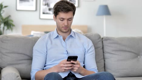 Hombre-joven-usando-smartphone-mientras-se-relaja-en-el-sofá