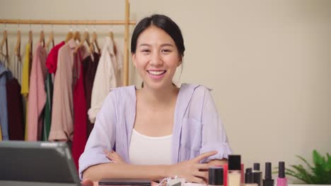 Beauty-Blogger-präsentieren-Beauty-Kosmetik-sitzen-vor-dem-Tablet-für-die-Aufnahme-von-Video.-Glücklich-schöne-junge-asiatische-Frau-verwenden-Kosmetik-Rezension-Make-up-Tutorial-übertragen-Live-Video-an-soziale-Netzwerk.