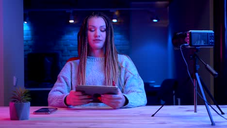 Closeup-shoot-of-young-attractive-female-blogger-with-dreadlocks-playing-video-games-on-the-tablet-getting-emotional-streaming-live-live-with-the-neon-background-indoors