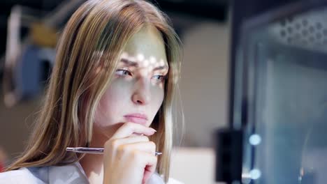 Closeup-of-beautiful-female-engineer-standing-near-3d-printer-in-laboratory,-observing-three-dimensional-printing-process,-making-notes-with-pen-and-thinking