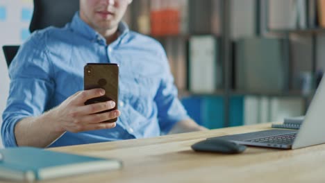 Businessman-Sitting-at-His-Desk-Works-on-Desktop-Computer-in-the-Stylish-Office,-Picks-up-and-Starts-Using-Smartphone,-Uses-Social-Media-App,-Emailing-Business-Partners,-Messaging.-Focus-On-Hands-and-Phone