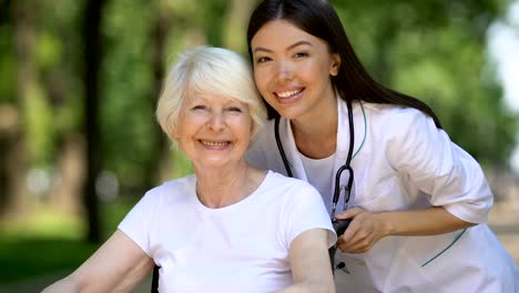 Cheerful-woman-in-wheelchair-and-doctor-showing-thumbs-up-smiling-to-camera