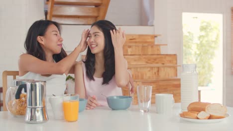 Asian-Lesbian-couple-has-breakfast-drink-juice,-cereal-and-milk-in-bowl-on-table-in-kitchen-at-home.