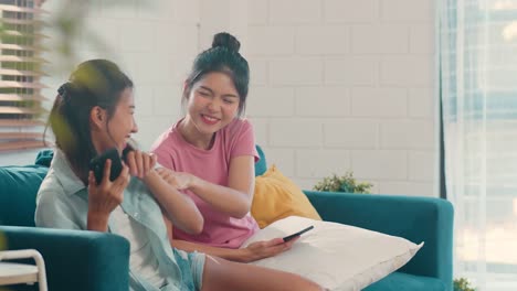 Young-Asian-Lesbian-women-couple-using-mobile-phone-check-social-media-on-internet-together-while-lying-sofa-in-living-room.