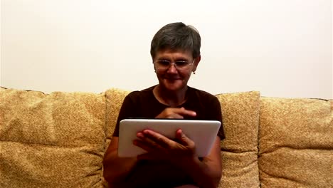 Attraktive-erwachsene-Frau-arbeiten-auf-ihrem-Tablet,-während-auf-einem-Sofa-zu-Hause-sitzen.