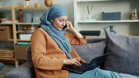 Cámara-lenta-de-la-empresaria-musulmana-hablando-por-teléfono-móvil-usando-computadora-portátil-en-casa