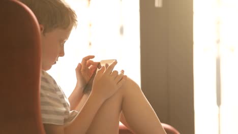 Boy-sitting-in-armchair-with-tablet-PC-playing-games.