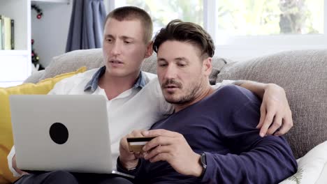 Gay-couple-relaxing-on-couch-using-laptop-computer.-Online-shopping.