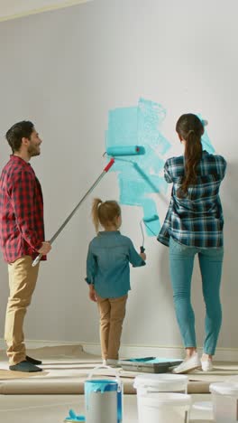 Disparo-de-espalda-de-una-familia-pintando-paredes-con-su-pequeña-hija-linda.-Pintan-con-rodillos-que-están-cubiertos-de-pintura-azul-claro.-Sala-Renovations.Video-Footage-con-Orientación-Vertical-de-pantalla-9:16