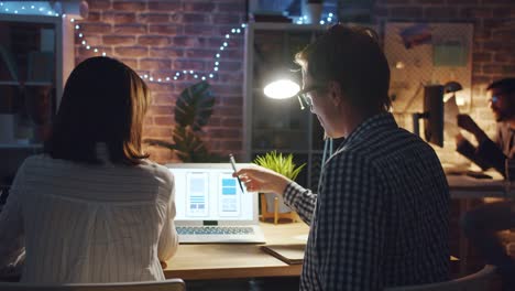 Man-and-woman-smartphone-app-designers-talking-in-office-working-with-laptop