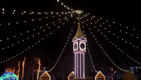 Clock-tower-decorated-with-Christmas-lights,-bulb-garlands-on-city-square-New-Year-market.-Camera-flies-around-decorative-Big-Ben-on-Christmas-Eve.-Time-and-holidays-concepts