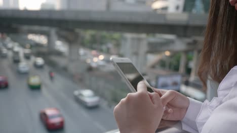 De-cerca-Mano-de-mujer-de-negocios-utilizando-el-teléfono-inteligente-en-el-centro-de-la-ciudad-moderna-en-la-noche-de-Bangkok-Tailandia.-Comunicación-Concept-Technology-por-teléfono-móvil