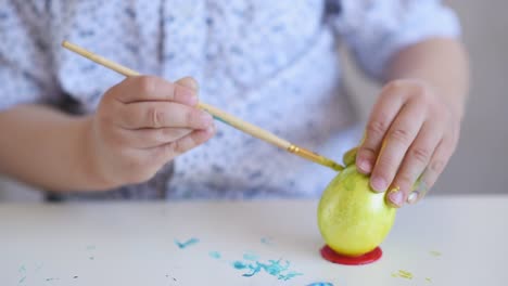 The-hands-of-a-litlle-child-paint-an-Easter-egg-in-yellow-color-on-a-stand.