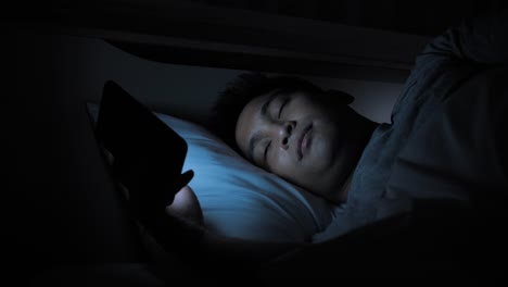 Nahaufnahme-asiatische-männliche-Mit-Smartphone-auf-dem-Bett-in-der-Nacht-zu-Hause