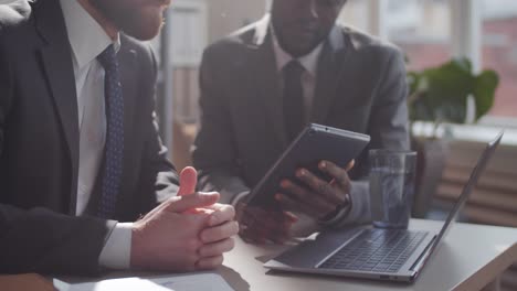 Two-Multiethnic-Business-Partners-Using-Tablet-and-Talking-at-Office-Desk