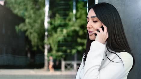 Asian-girl-talking-use-mobile-outdoor-at-glass-wall-building.-Medium-close-up-shot-on-4k-RED-camera