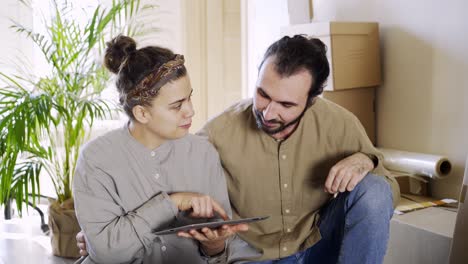 Paar-mit-Tablet-in-neuer-Wohnung-in-der-Nähe-von-Stapel-von-Boxen