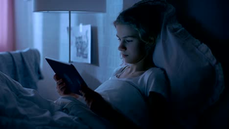 Young-Teenage-Girl-Lies-in-Her-Bed-at-Night-With-Tablet-Computer.-Watches-TV-Show.