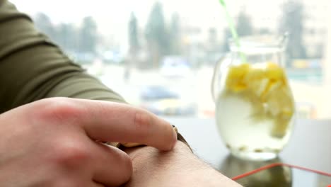 Closeup-view-of-man-checking-for-notifications-on-smartwatch-while-sitting-at-table-with-lemonade-pitche