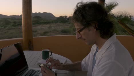 Man-scrolling-through-smart-phone-at-home-office-by-ocean-looking-at-email