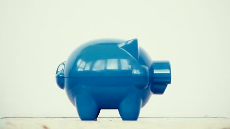 Blue-piggy-bank-and-a-person-adding-coins