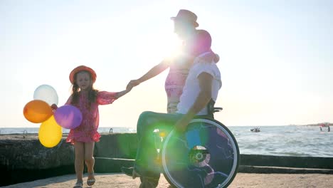 glückliche-Familie,-Behinderte-im-Rollstuhl-spazieren-mit-schwangere-Frau,-Kind-hält-Luftballons-und-springen,-mit-Frau-ungültig