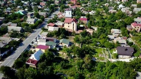 Video-from-the-drone.-View-from-high-to-a-car-that-rides-along-an-asphalt-road-in-a-small-suburban-village.-The-camera-moves-down-above-the-roofs-of-houses.