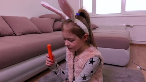 Little-girl-watching-decorative-Easter-egg-and-eating-carrot