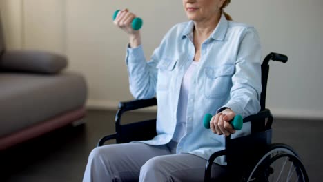 Elderly-female-in-wheelchair-lifting-dumbbells-at-rehabilitation-center,-trauma