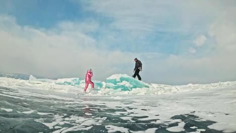 Pareja-joven-tiene-diversión-durante-el-invierno-a-pie-contra-el-fondo-de-hielo-del-lago-congelado.-Los-amantes-son-sentados-en-grandes-témpanos-azules,-besos-y-abrazos,-beber-el-té-del-termo.-Historia-de-amor.