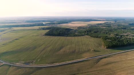 Flight-above-countryside-green-fields,-forest,-and-village-early-spring,-aerial-panoramic-view.