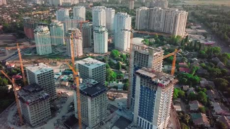 Aerial-drone-shot.-Construction-of-high-rise-buildings-in-the-developing-area-of-a-large-city.-In-the-picture,-construction-cranes-and-many-houses-under-construction.-Camera-moves-down