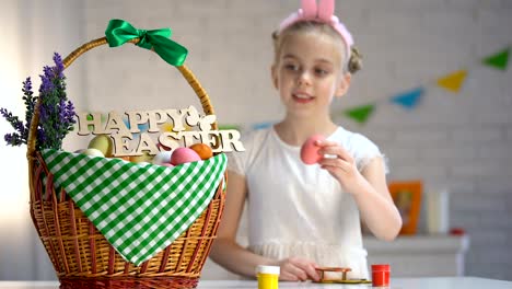 School-girl-painting-and-putting-colored-egg-in-basket,-holiday-atmosphere