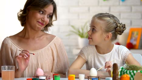 Mother-watching-daughter-painting-Easter-egg-for-first-time,-family-traditions