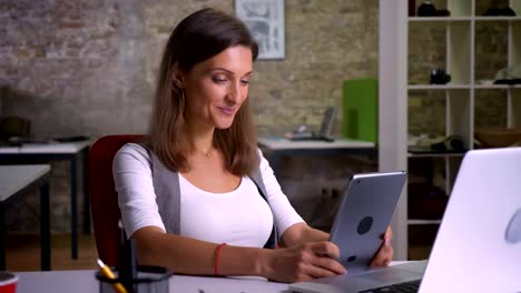 Attractiver-female-office-worker-browsing-on-the-tablet-smiling-on-the-workplace-indoors