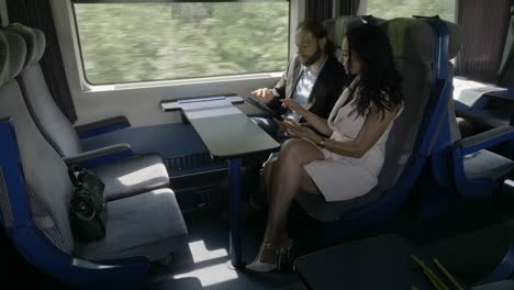 Young-corporate-couple-man-and-woman-discussing-about-business-project-using-their-device-tablet-pc-and-smartphone-while-they-traveling-by-train