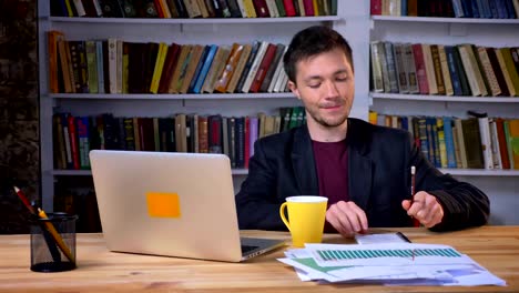 Attractive-adult-businessman-taking-notes-next-to-the-laptop-and-drinking-coffee-with-a-happy-and-satisfied-facial-expression