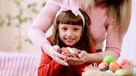 mom-and-daughter-are-smiling-broadly,-holding-out-their-hands-with-Easter-eggs-to-the-camera.