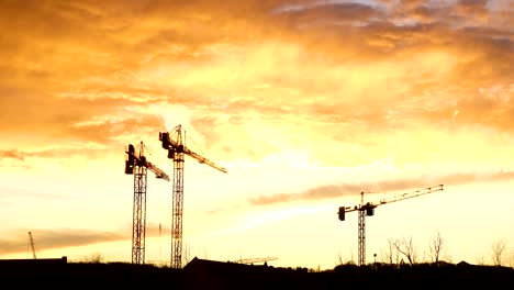 Baukräne-Silhouetten-bei-rotem-bewölktem-Sonnenuntergang