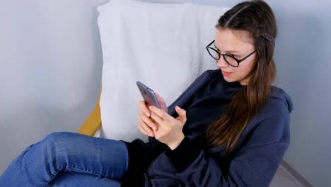 Jovencita-morena-en-gafas-está-jugando-juego-en-el-teléfono-móvil.