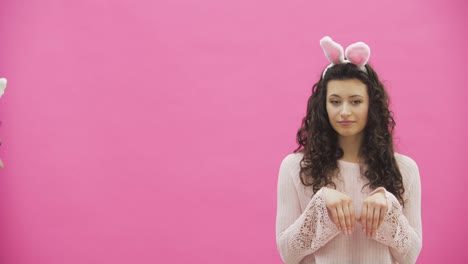 Joven-hermosa-pareja-de-pie-sobre-un-fondo-rosa.-Durante-esto-hacen-movimientos-de-conejos.-La-mujer-puso-sus-manos-en-su-cuello.-Vistas-suaves-y-toques-entre-sí.-En-las-orejas-de-conejo-de-la-cabeza.