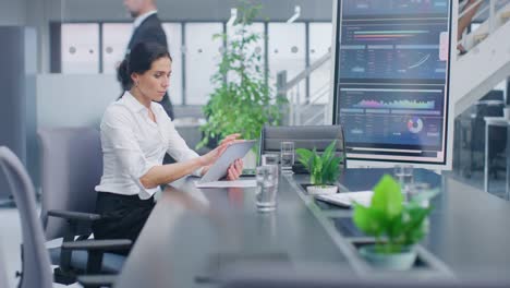 Im-Besprechungsraum-setzt-sich-confident-Female-Executive-am-Konferenztisch-mit-digitalem-Tablet-Computer,-analysiert-Statistiken,-schaut-auf-Handelszahlen-und-Investitionsmöglichkeiten.-Im-Corporate-Office