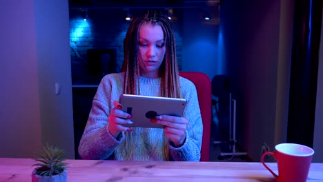 Closeup-shoot-of-young-attractive-female-blogger-with-dreadlocks-playing-video-gameson-the-tablet-winning-and-being-happy-streaming-live-with-the-neon-background-indoors