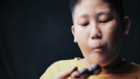 large-build-Asian-preteen-boy-eating-donut-while-touching-his-tummy,-slow-motion-in-low-light.