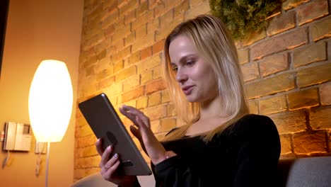 Nahwärtsseite-Blick-Porträt-der-jungen-hübschen-Hausfrau-mit-dem-Tablet-und-sitzen-auf-der-Couch-drinnen-in-gemütlichem-Haus