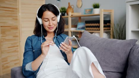 Female-student-enjoying-music-through-headphones-touching-smartphone-screen