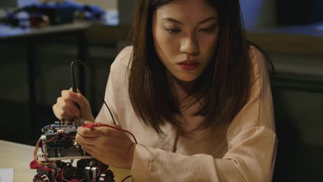 Young-asian-female-electronics-development-engineers-works-with-robot,-measuring-the-signal-in-the-electrical-circuits-of-robotics-prototype-in-workshop.-People-with-technology-or-innovation-concept.