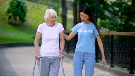 Female-volunteer-supporting-sick-old-woman-walking-frame,-rehab-difficulties